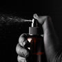 Hand wearing a glove holding a spray bottle with a dark background