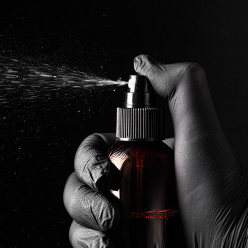 Hand wearing a glove holding a spray bottle with a dark background
