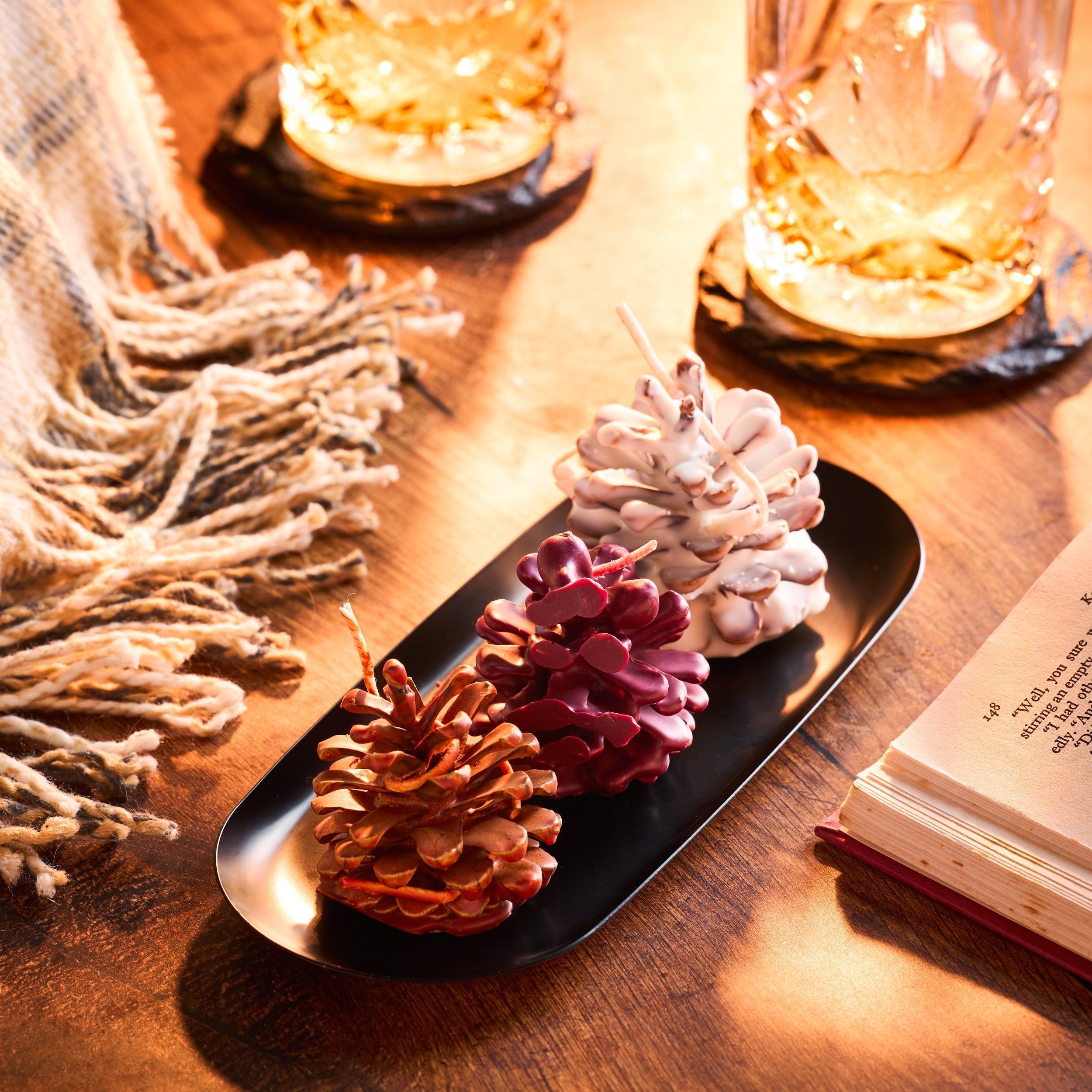 Wax covered pinecones on a tray next to glasses and a blanket