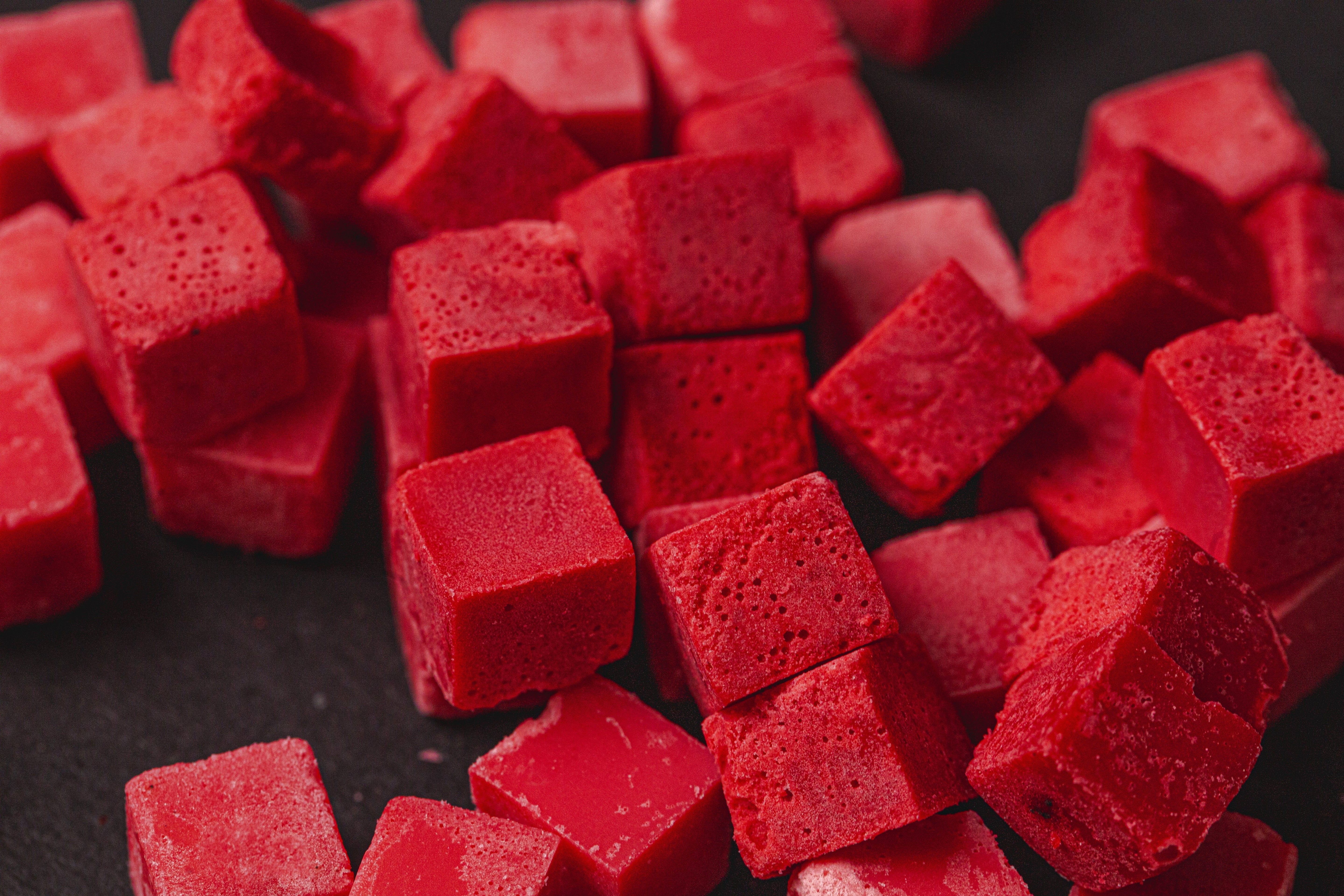 Close-up of vibrant red candle dye chips in small cube form, showing their textured surfaces and rich color on a dark background.