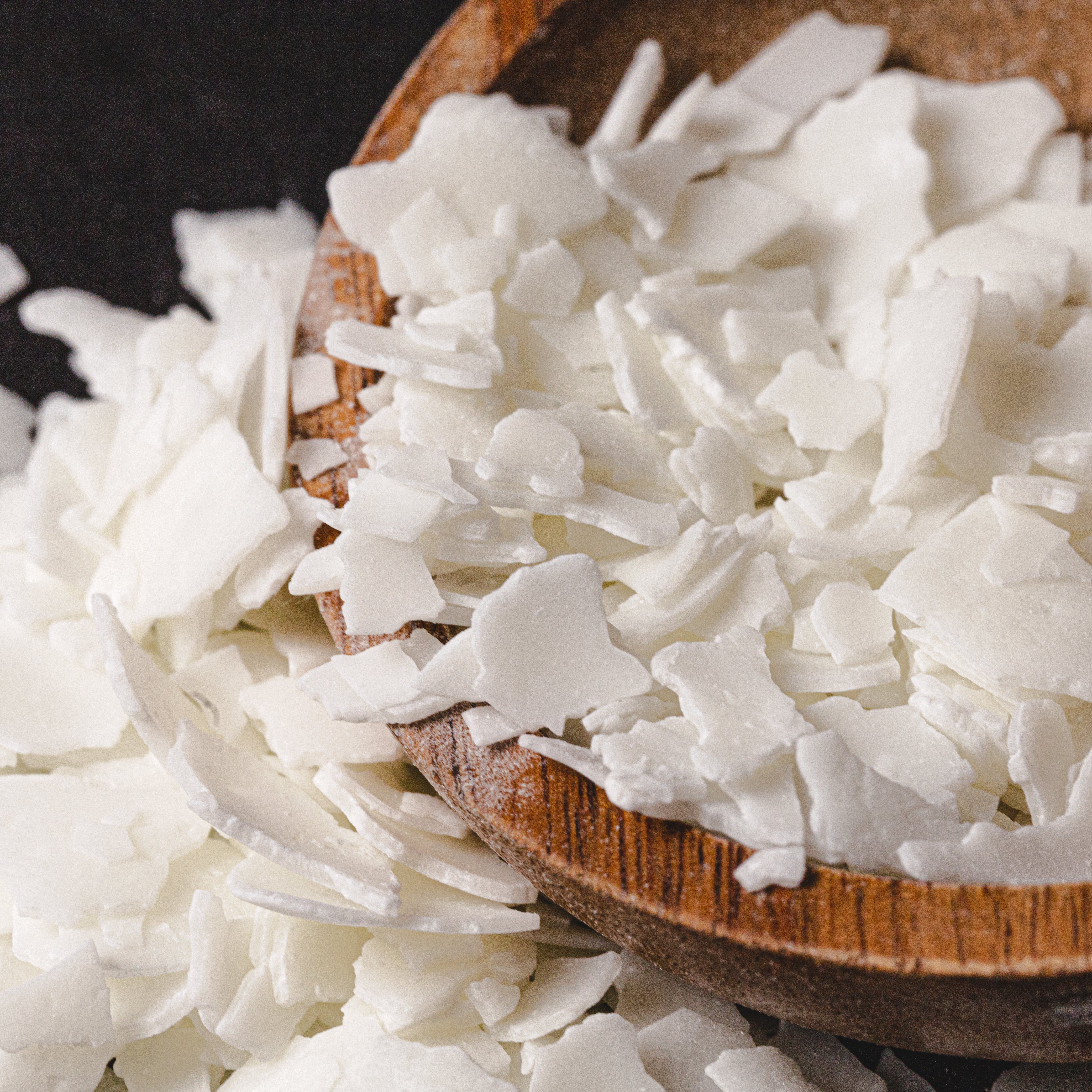 Close-up of natural soy wax flakes in a wooden bowl, showcasing their smooth, white texture and delicate, layered appearance.