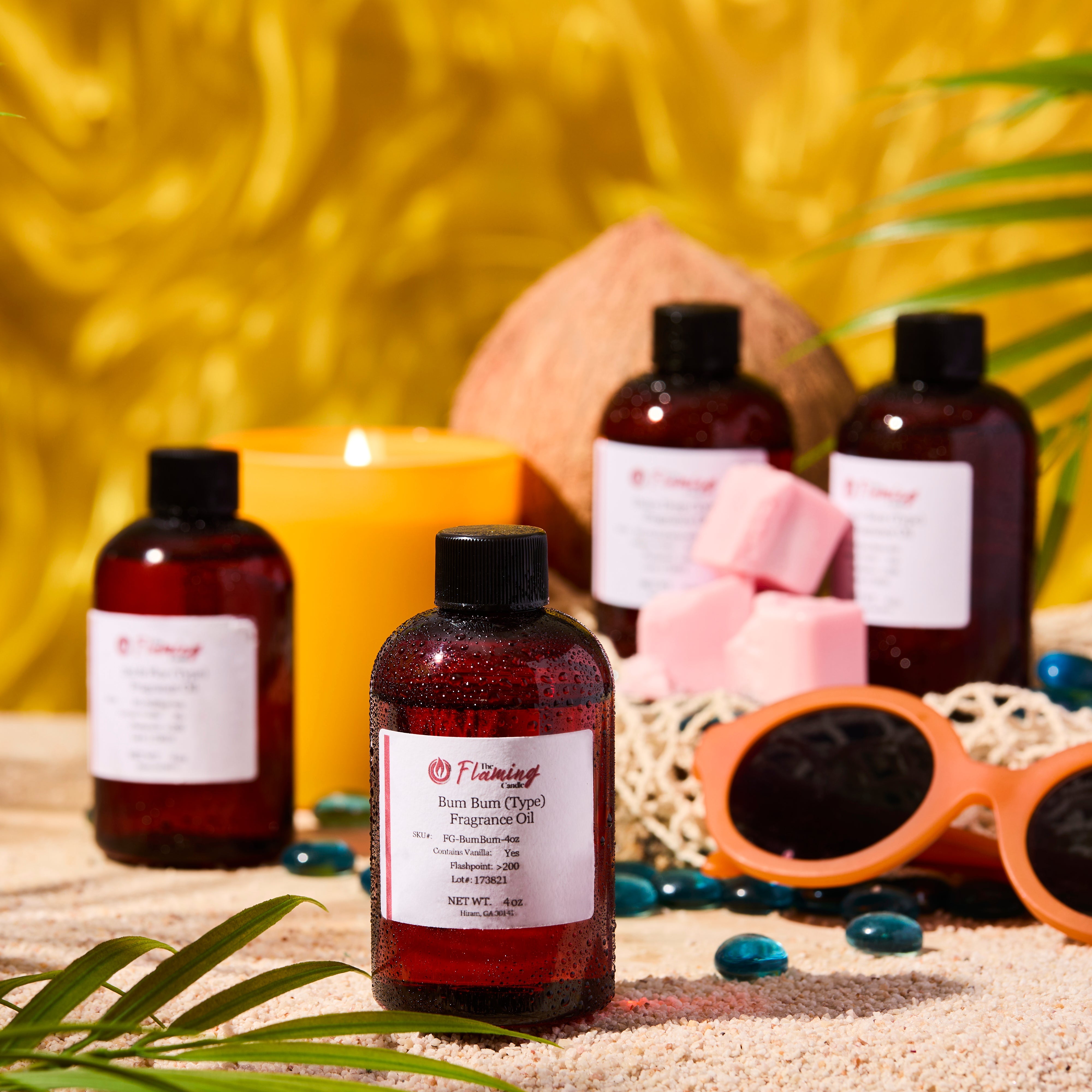 Summery beach-themed scene featuring The Flaming Candle “Bum Bum (Type)” fragrance oils with condensation, a yellow candle, pink wax melts, coconut, sunglasses, and palm leaves on sand against a golden background.