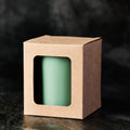 Green candle in a brown cardboard box with a window on a dark background