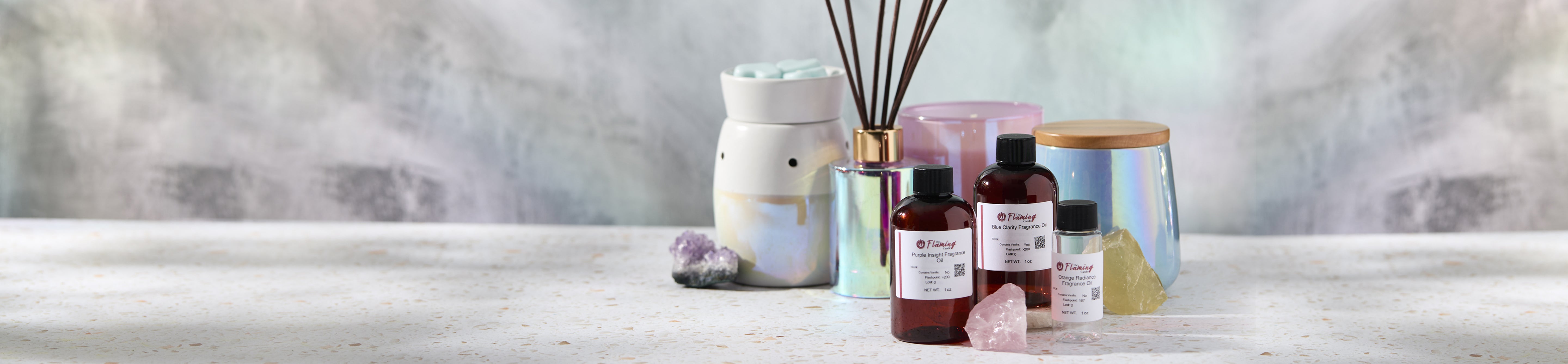 Iridescent candle making setup with diffuser reeds, a wax warmer, and amber fragrance oil bottles arranged with crystals on a light stone surface.