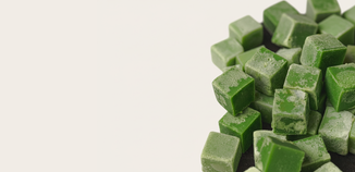 Close-up of green dye chips for candle making scattered on a light surface.