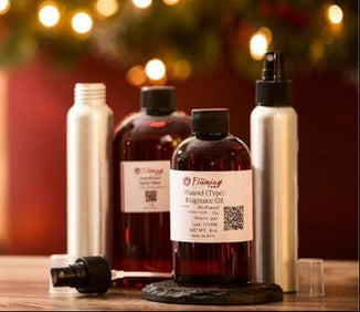 A festive room spray kit featuring The Flaming Candle fragrance oils and aluminum spray bottles, styled on a wooden surface with soft holiday lights and greenery in the background.