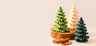 Three Christmas tree candles in light green, ivory, and dark green arranged with a wooden riser, dried orange slices, and cinnamon sticks.