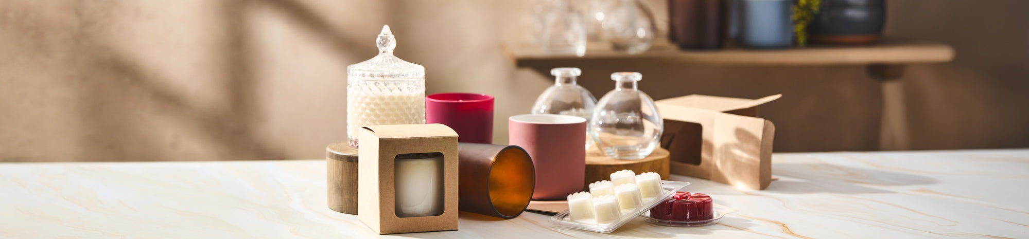 Arrangement of candles and wax melts in glass jars and kraft boxes on a marble surface, with wooden stands and neutral-toned background, styled as a product display for handmade or home fragrance items.