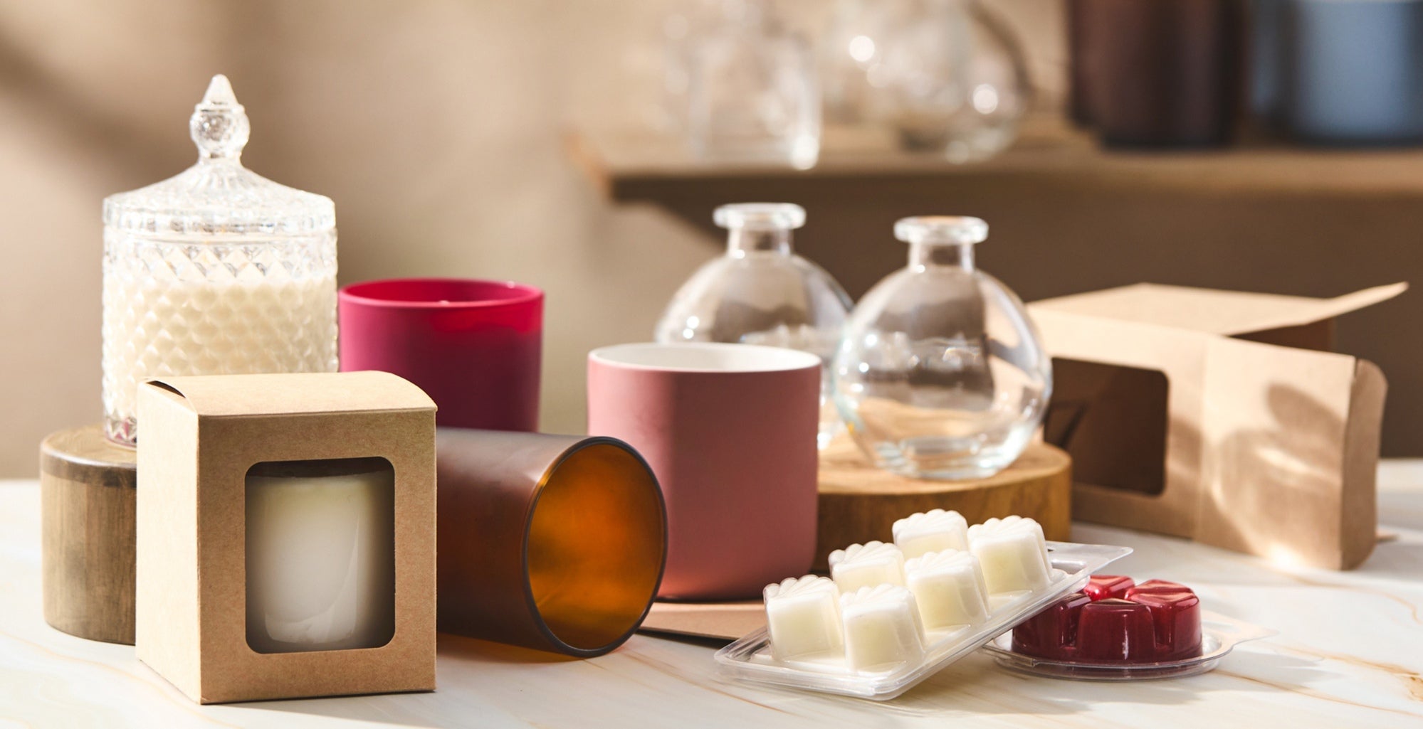 Arrangement of candles and wax melts in glass jars and kraft boxes on a marble surface, with wooden stands and neutral-toned background, styled as a product display for handmade or home fragrance items.