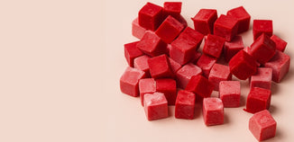 A pile of vibrant red candle dye chips scattered on a soft neutral surface, showcasing their rich color and smooth, waxy texture.