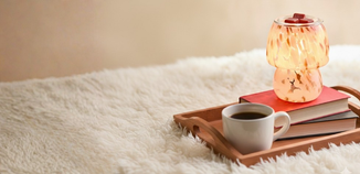 Lighted mushroom-shaped art glass wax warmer with red wax melts on top, styled on stacked books with a coffee cup nearby.