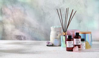 The Flaming Candle fragrance oil bottles styled with reed diffuser reeds, wax melts, and iridescent candle containers—DIY candle making and home fragrance supplies on a pastel backdrop.