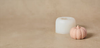 White silicone pumpkin-shaped candle mold beside a finished pumpkin-shaped candle on a neutral beige background.