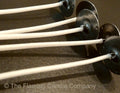 Close-up of candle wicks with metal holders on a dark background, branded 'The Flaming Candle Company'.