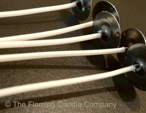Close-up of candle wicks with metal holders on a dark background, branded 'The Flaming Candle Company'.