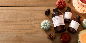 Amber bottles of fall-themed fragrance oils, including Toasted Vanilla Pumpkin, arranged on a rustic wooden table with mini pumpkins, pinecones, and lit candles creating a warm autumn atmosphere.