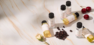 Assorted fragrance oil sample bottles arranged on a marble surface with coffee beans, cherries, a white rose