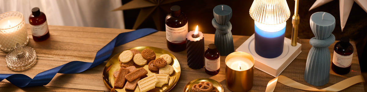 Lit candles, sculptural blue candles, fragrance oils, cookies on gold plates, and blue and gold ribbons arranged on a warmly lit wooden table.