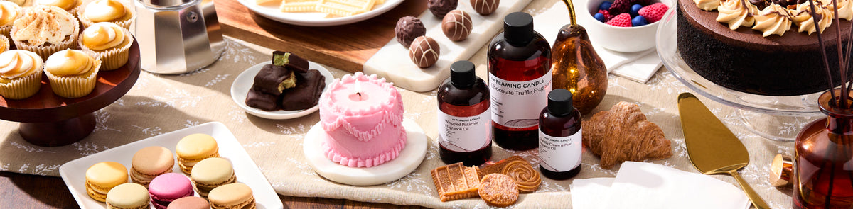 Dessert table with cupcakes, macarons, chocolates, croissants, a chocolate cake, and a pink cake-shaped candle, surrounded by dessert-scented fragrance bottles.